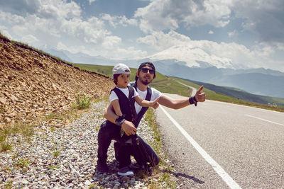 Father and son in caps and sunglasses catch a car standing on the road in the mountains