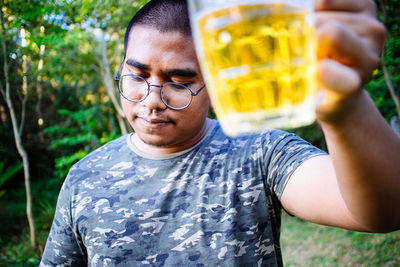 Portrait of young man holding eyeglasses standing outdoors