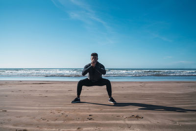 Full length of man exercising on beach against sky
