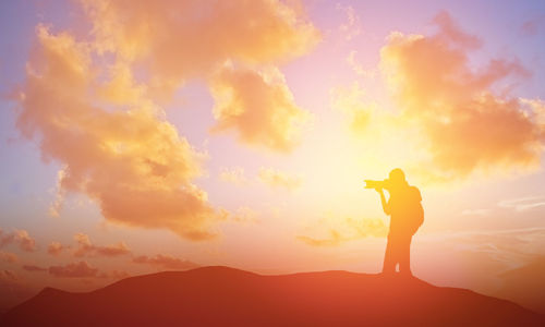 Silhouette woman photographing against sky during sunset