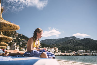 Woman sitting by mountain against sky