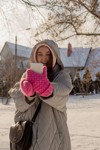 Woman with freckles in winter clothes with mittens outdoors uses her smartphone 