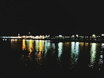 Illuminated city by river against sky at night