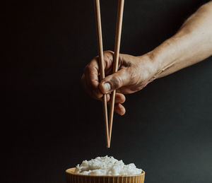 Close-up of hand holding chopsticks against black background