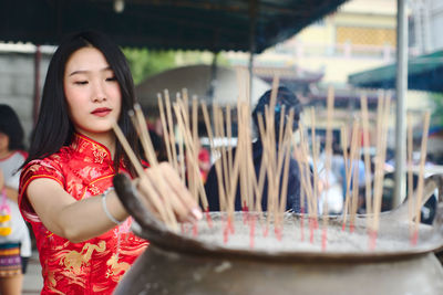 Close-up of young woman putting incense in container at temple