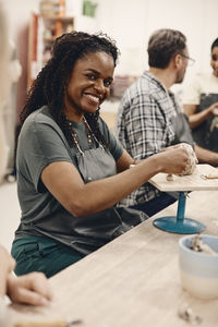 Portrait of happy mature woman molding clay sitting by man at table in art class