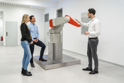 Engineer explaining robotic arm to colleagues standing at factory