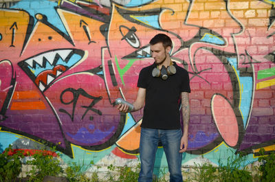 Full length of young man standing against graffiti wall