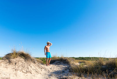 Full length of a man standing on beach against clear blue sky