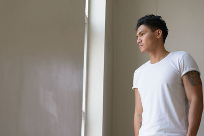 Young man looking away while standing against wall