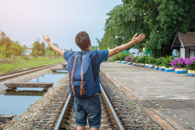 Rear view of man standing with arms outstretched standing on railroad track