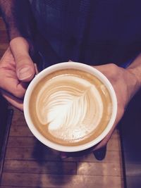 Close-up of hand holding cappuccino served on table