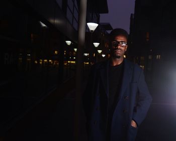 Portrait of man standing by illuminated lamp at night