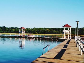 Pier by swimming pool by lake against clear sky