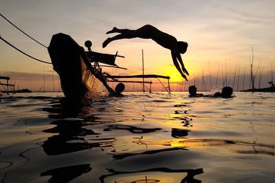 Silhouette men on beach against sky during sunset