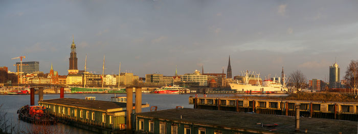 Buildings at waterfront against cloudy sky