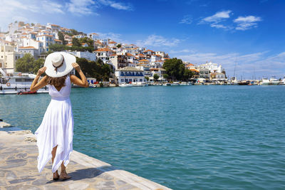 Rear view of woman with arms raised standing by sea against sky