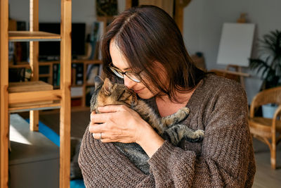 Middle-aged woman hugging cute tabby cat in indoor scene. human-animal relationships. funny home pet