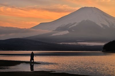 Rear view of man standing on mountain against sky during sunset