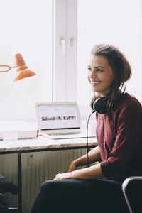 Confident mid adult businesswoman looking away while sitting at desk in creative office