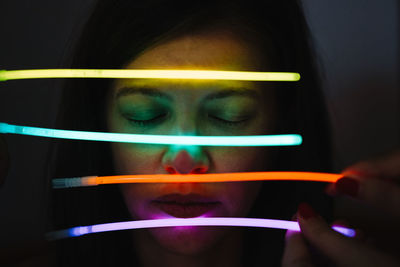 Close-up portrait of woman with neon sticks against black background