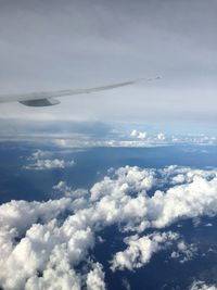 Aerial view of aircraft wing over clouds against sky
