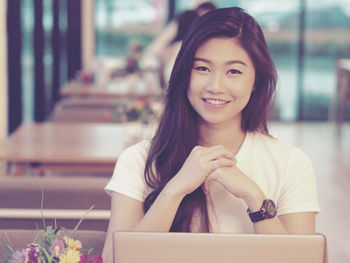 Portrait of smiling woman using laptop while sitting at restaurant
