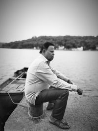 Side view of man sitting on pier against sky