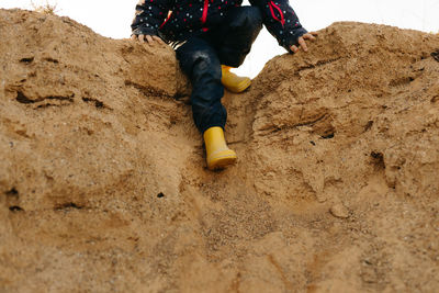 Child with yellow rubber boots playing on sand