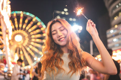 Smiling woman with sparkler standing in illuminated city at night
