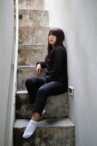 Side view of young woman sitting on wall