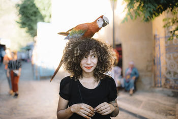 Young woman with macaw on head in city