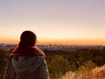 Rear view of man looking at cityscape against sky during sunset