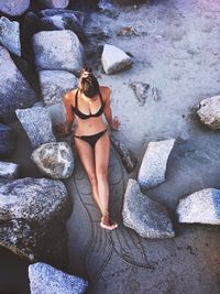 High angle view of young woman in bikini while sitting on rock