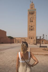 Rear view of woman standing by building against clear sky