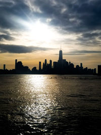 Silhouette buildings by sea against sky during sunset