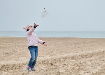 Young girl is playing on an empty beach during a foggy, cold day