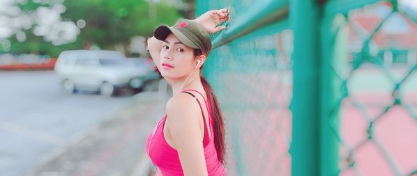 Portrait of young woman listening music while standing by chainlink fence