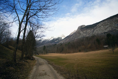 Dirt road along trees and landscape against sky