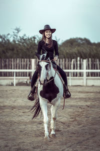 Portrait of woman sitting on horse in ranch against sky