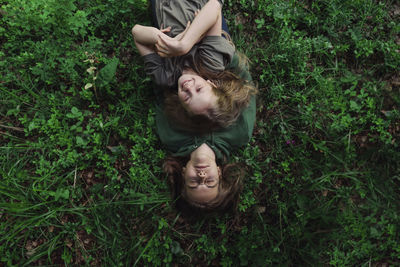 High angle view of sisters lying on grassy field in forest