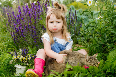 Sad girl holding cat while sitting amidst plants