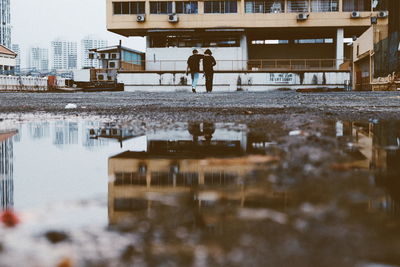 Reflection of man walking in puddle on city during winter