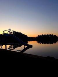 Silhouette swimming pool by lake against clear sky