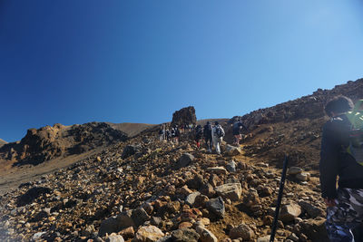People on rocks against clear blue sky