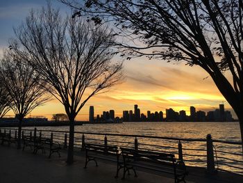 Silhouette bare tree by buildings against sky during sunset