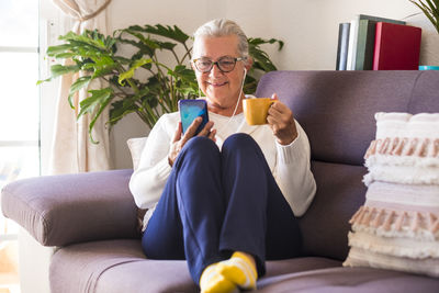 Full length of senior woman holing coffee cup talking on video call at home