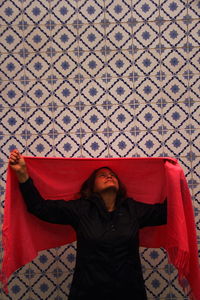 Woman holding red scarf against pattern wall