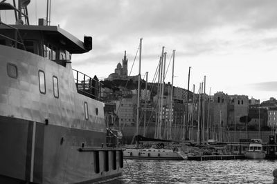 Sailboats moored on harbor by buildings against sky