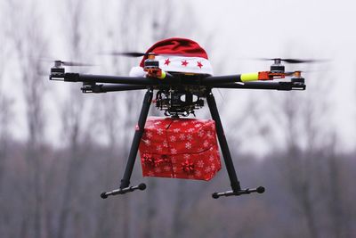 Drone with santa hat carrying christmas present against sky